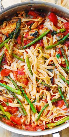 pasta with asparagus and tomatoes in a pan on a wooden table, ready to be eaten