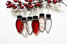 three red and white earrings hanging from a branch with berries in the background on a white surface