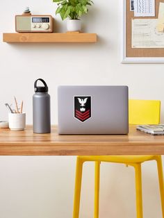 a laptop computer sitting on top of a wooden desk next to a yellow chair and potted plant