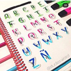 an open notebook with letters and numbers drawn on the pages, surrounded by crayons