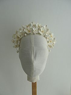 a white headdress with flowers on a wooden stick in front of a white wall