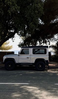 a white land rover is parked on the side of the road next to some trees