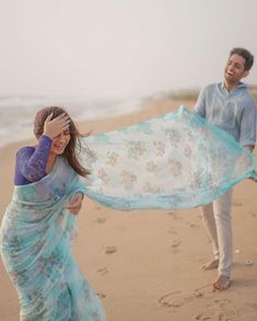 a man and woman walking on the beach with a blue shawl over their heads