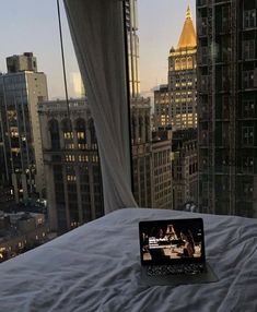 an open laptop computer sitting on top of a bed in front of a city skyline