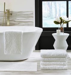 a white bath tub sitting next to a window with flowers in vases on the side