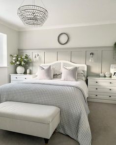 a bedroom with a white bed, dressers and a chandelier