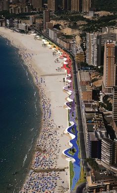 an aerial view of a beach with many people on it and buildings in the background