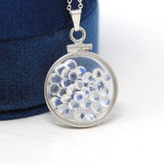 "Magical handcrafted brand new sterling silver genuine moonstone shaker locket! This whimsical pendant is dime sized with coin style bezels, and clear lucite covers. The round charm hangs from a brand new sterling silver chain, and is filled with approximately 2.5 carats of cabochon and round cut moonstone gems. An otherworldly piece of brand new gemstone jewelry, that features the optical phenomenon; adularescence! ERA - New METAL / MATERIAL - Sterling silver locket, sterling silver chain, luci Moonstone Round Pendant Jewelry For Gift, Round Labradorite Moon Phase Necklace, Labradorite Moon Phase Round Necklace, Moonstone Round Necklace For Anniversary, White Gold Moonstone Round Pendant Jewelry, Silver Moon-shaped Locket Jewelry, Silver Moonstone Round Pendant Jewelry, Unique Moonstone Round Pendant Jewelry, Sterling Silver Moon Phase Jewelry