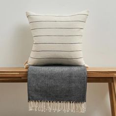 a black and white striped pillow sitting on top of a wooden table next to a gray blanket