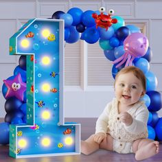 a baby sitting in front of a number one balloon arch