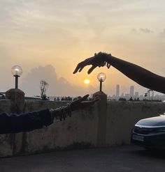 two people reaching out towards each other in front of a car with the sun setting behind them