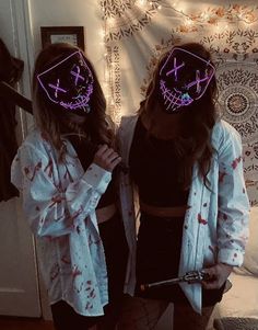 two girls wearing scary masks in front of a wall with lights on it and one girl holding a knife