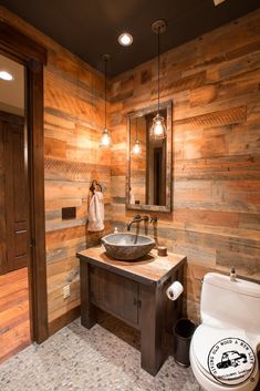 a bathroom with wooden walls and flooring has a toilet, sink, and mirror