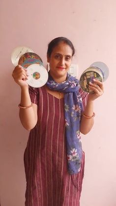 a woman holding two plates in one hand and a blue scarf on the other, standing against a pink wall