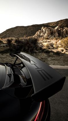 the back end of a sports car parked in front of a rocky mountain side area