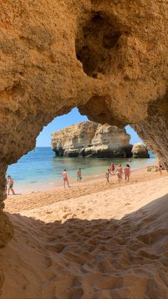 people are walking on the beach under some rocks