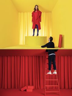 a man standing on top of a red and yellow stage next to a woman in a red coat