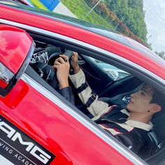 a young man sitting in the driver's seat of a red car while holding a cell phone