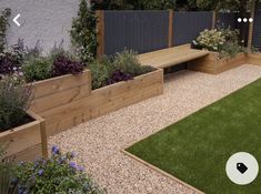 a garden with wooden planters, grass and flowers on the side of the building