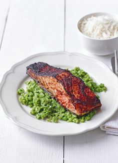 a white plate topped with meat and peas next to a bowl of rice on top of a table