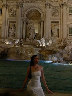 a woman standing in front of a fountain at night