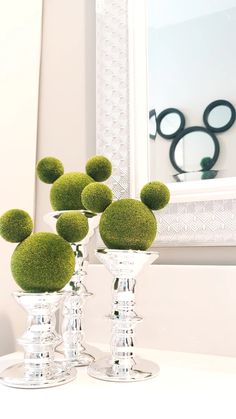 four glass vases with moss balls in them on a white table next to a mirror