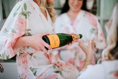 two women in robes are holding champagne bottles and smiling at each other while another woman holds a bottle