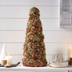 a christmas tree made out of pine cones on a mantle next to candles and plates