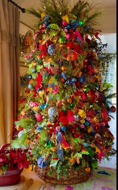 a very colorful christmas tree with ornaments on it's branches and decorations around the base