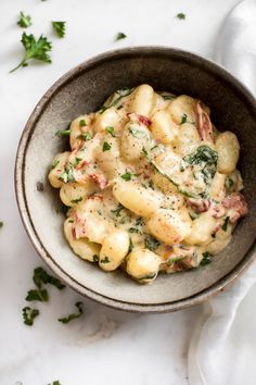 a bowl filled with pasta covered in cheese and spinach sprinkled with parsley