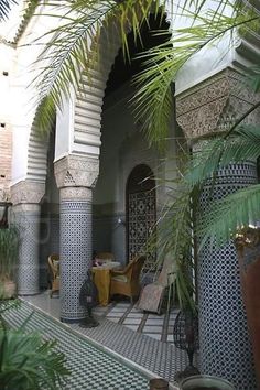 an outdoor courtyard with potted plants and chairs on the floor, surrounded by palm trees