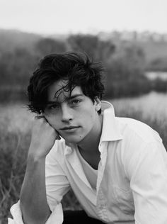 black and white photograph of a young man sitting in a field with his hands on his head