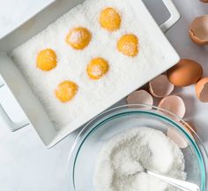 eggs and flour in bowls on a white counter with utensils next to them