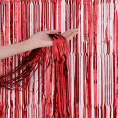 a person holding something in their hand with red and white strips on the wall behind them