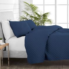 a bed with a blue comforter and pillows on it in front of a window