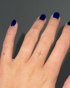 a woman's hand with blue nail polish and a star tattoo on her ring finger