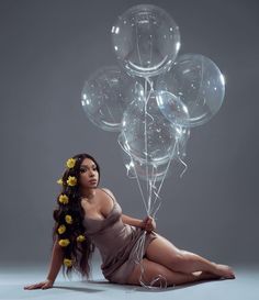 a woman sitting on the ground with some balloons in her hand and flowers in her hair