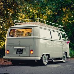 an old vw bus is parked on the side of the road in front of some trees