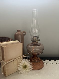 an old fashioned lamp, book and vase on a lace doily with a white flower