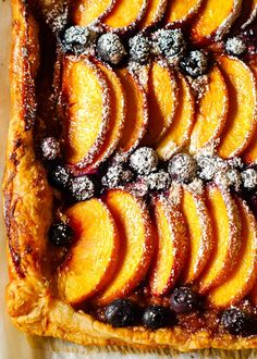 a pastry topped with sliced peaches and blueberries on top of a white table