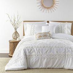 a bed with white comforter and pillows in a room next to a vase filled with flowers