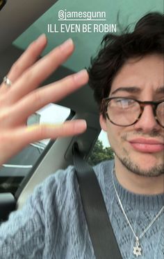 a man wearing glasses and holding his hand up in the back seat of a car