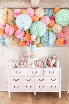 a white dresser topped with lots of colorful paper balls and cake on top of it