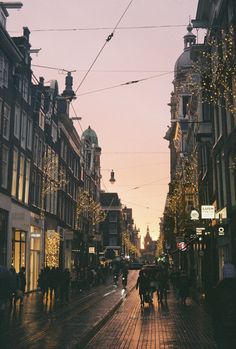 people are walking down the street with lights strung over them and buildings in the background