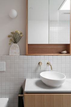 a white sink sitting under a bathroom mirror next to a wooden cabinet and counter top