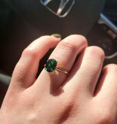 a woman's hand with a green ring on top of her finger in a car