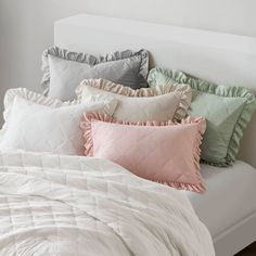 a bed topped with lots of pillows next to a white headboard covered in blankets