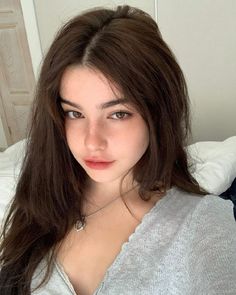 a young woman with long brown hair posing for the camera in her bedroom, wearing a gray shirt