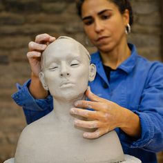 a woman is working on a clay head