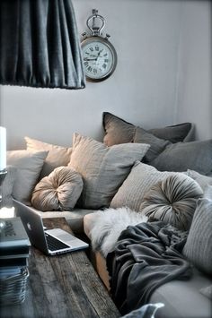 a laptop computer sitting on top of a wooden table in front of a couch covered with pillows